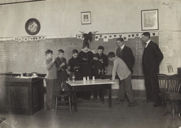 Teachers and students using a "Babcock Tester" in a classroom. Original caption reads: "Pupils of grammar grades testing milk with Babcock Tester; County Superintendent Tobin and rural life leader Phillips, looking on."