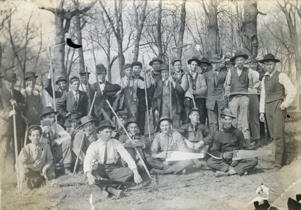 Group of boys outdoors with gardener E.E. Harris. Original caption reads: "Boys of the Onalaska Agricultural School, with rakes and forks, saws and other implements, ready for a day in the field."
