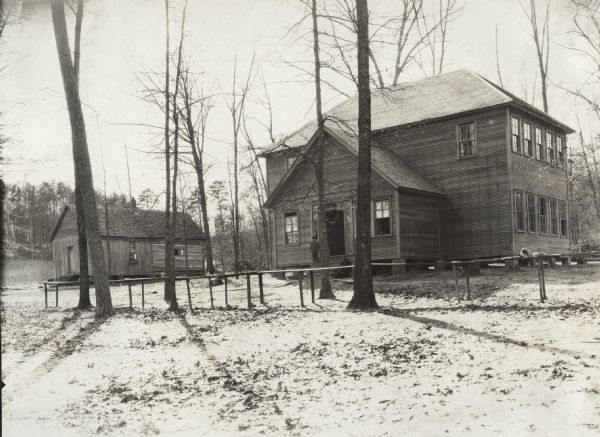 Alabama school buildings. A young boy stands on the steps of the new building. Original caption reads, "A comparison of old and new school buildings at Pleasant Hill, seven miles from Decatur. At the left is shown the original log school house, as the farther half of the building. It was 12 feet square and had three small windows and a door. Later the building was increased in size by adding a frame room on the end, with large windows. At right is shown the new building which has two recitation rooms and clothes closets on the first floor and the upstairs is for use of Odd Fellows Lodge and community meetings. Provision has been made for painting the building, the entire cost of construction being about $1300. The long table in front is for basket picnics, in connection with their community meetings and on Sunday when they hold service at the church near by."