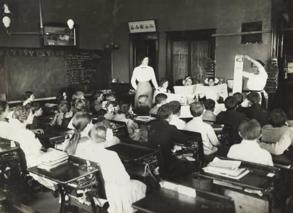 Teacher explaining seed germination test ("rag doll" test) to her students. Original caption reads: "Mrs. Agnes Ryan Page explaining the Rag Doll Test to her boys and girls."