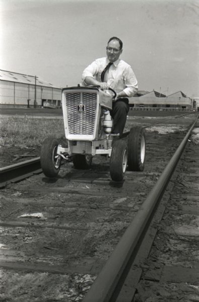 A man drives an International Harvester Cub Cadet along the inside of railroad tracks to test the machine. The photograph was probably taken outside of International Harvester's Louisville Works factory.