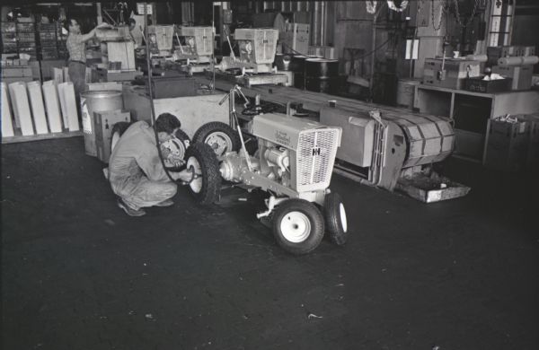 A man attaches wheels to an International Cub Cadet lawn tractor at the company's Louisville Works factory. Other men are working in the background.
