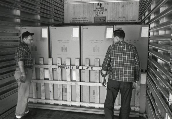 Factory workers load boxes of International Harvester Cub Cadet lawn tractors made at Louisville Works into a truck. The boxes are held in place by a wooden barrier with text that reads, "Property of L & N."
