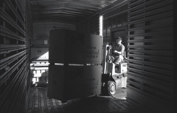 View from inside of a railroad car of a factory worker using a forklift to load International Cub Cadet lawn tractor boxes onto wooden pallets at the company's Louisville Works.