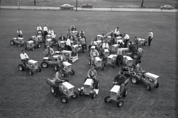 Elevated view of men, possibly dealers or buyers, sitting on and gathered near International Harvester Cub Cadet lawn tractors. The machines were manufactured at the company's Louisville Works.