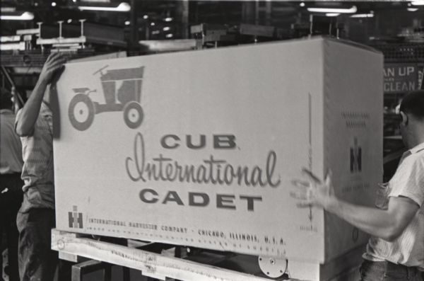 Two men lift an International Cub Cadet lawn tractor box onto a wooden pallet in preparation for a shipment from the Louisville Works factory by train.