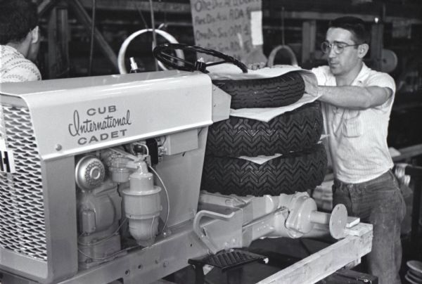 A factory worker stacks tires on a Cub Cadet lawn tractor as he readies it for shipment from International Harvester's Louisville Works. The machine will be boxed for delivery by rail and the tires will be attached when they reach the dealership.