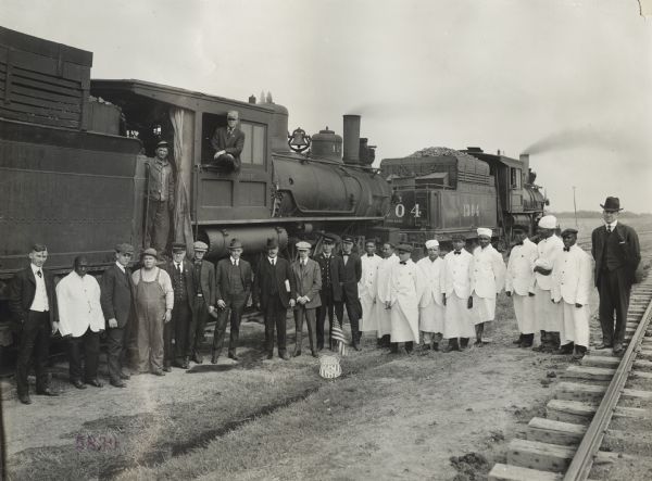 Large group of men, including railway workers, standing beside a locomotive. Original caption reads: "U.P. Nebraska Preparedness Special Campaign. Farm preparedness special crew." A small American flag is posted on the ground in front of them, behind a shield that says: Union Pacific System -- The Overland Route."