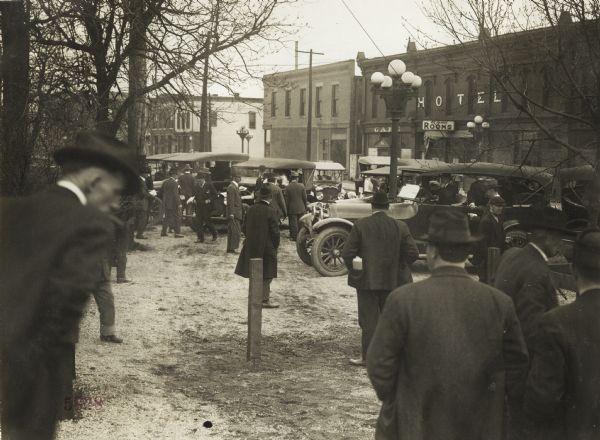 Group of men gathered with automobiles across the street from a hotel, small cafe and other town buildings. The men are gathering for an event associated with the Union Pacific Nebraska Farm Preparedness Special Campaign.