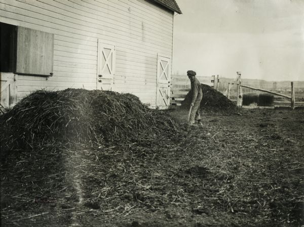 Young man outside a barn pitching piles of manure. Original caption reads: "Union Pacific Silo Special Trip. Manure, J.A. Butler."