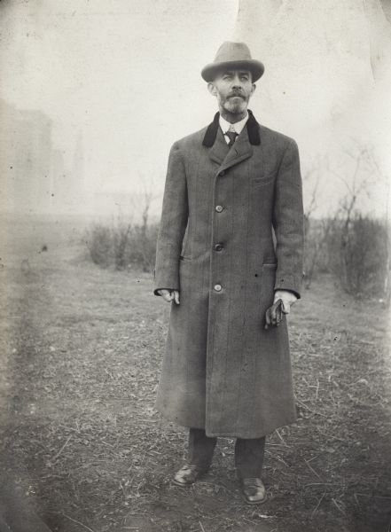 Professor Perry Holden standing outdoors in a tweed overcoat and fedora. Holden was in charge of International Harvester's Agricultural Extension Department.