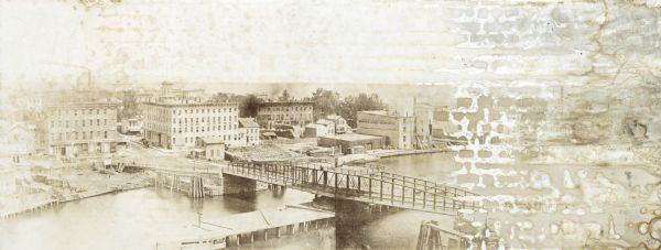Panoramic view of downtown Chicago before the fire of 1871. The photograph was taken from the South side of the Chicago River, looking Northeast. The Rush Street bridge (a "swing bridge") is in the foreground. On the far side of the river, partially obscured by damage to the original print, is the McCormick Reaper Works. The factory was destroyed in the fire of 1871. The other identified buildings are Oswego Mills Store, Lake House, and Marsh's Caloric Grain Dryer. Lake Michigan appears in the distance.