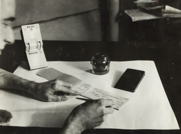 Close-up of a man writing a check for $4.35 to a "Henry Peterson." The check is dated at Chicago and is printed with the name "Merchants' Loan & Trust Company."