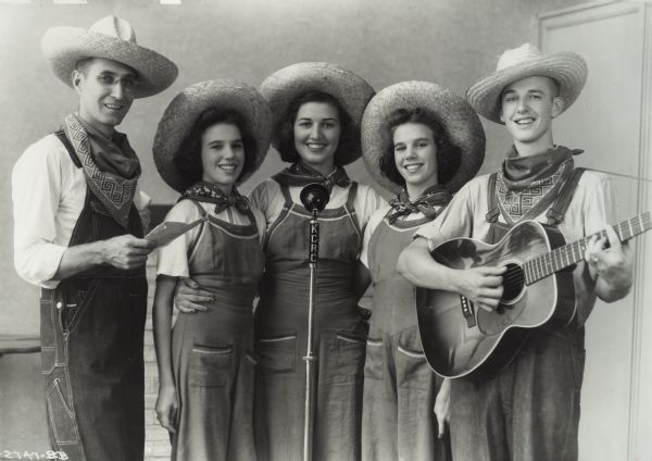 Group portrait of the McCormick-Deering Sisters and Big Brother Johnny, taken at the KCRC studios. Original caption reads: "Radio Talent "McCormick-Deering Sisters + Big Brother Johnny." Left to right, Ralph Rogers, announcer, Jean, Lon + Ginger Denning and Jo. K. Holke (Johnny.)