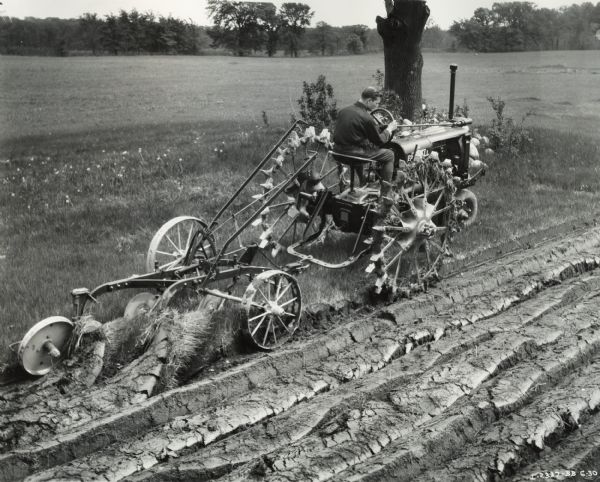 Man pulling a 2-row disk plow with a Farmall F-14 tractor. Original caption reads "Vincent E. Steele of Valparaiso, Indiana plowing 20 acre field of old sod with F-14 & 2 row (14" bottoms) plow. Also owns a 1 row potato planter and a cultivator."