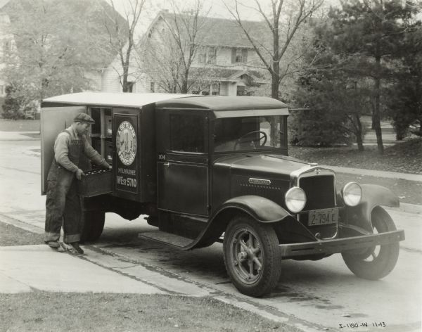 International delivery truck operated by A. Gettelman (brewery) of Milwaukee. A man in work clothes is standing near the side of the truck near an open door, holding a crate of bottles.