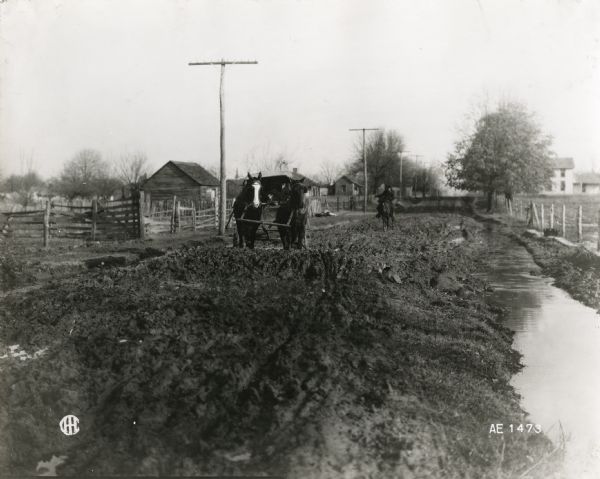 A mail carrier on horseback is approaching a stranded horse-drawn carriage along a stretch of poor quality rural road. Farmhouses and farm buildings are on either side. The ditch on the right is full of water.