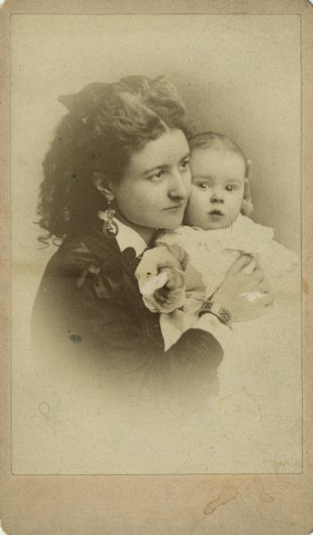 Vignetted carte-de-visite portrait of Mary Caroline Adams posing with one of her infant children cradled against her cheek.