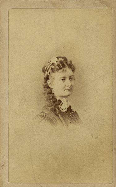 Vignetted carte-de-visite quarter-length portrait of Mary Caroline Adams Chapman (Mrs. John E.). She is wearing a necklace, earrings, and a decoration in her hair.