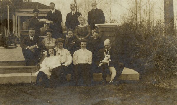 Group portrait of Adams family seated outdoors on patio of home. Group includes Cyrus H. Adams, Sr., Emma (Blair) Adams, Mary (Shumway) Adams, Ruth Campbell, Minnie (Adams) Campbell, Anna (Chapman) Dunn, and others.