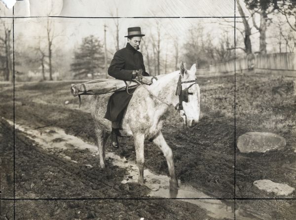 Agricultural Extension lecturer Dr. F.A. Wolfe carrying an educational chart while riding on horseback along a muddy dirt road.