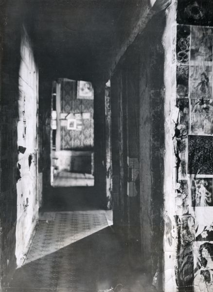 Interior view down a hallway at the Courtland Hotel. The walls are covered with peeling wallpaper and the floor is made of patterned tile. The hotel was used by Agricultural Extension lecturers as they passed through on a tour of Alabama.