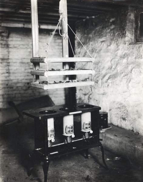 A wooden drying rack is hanging from the ceiling over a gas stove in what appears to be a cellar or a shed.