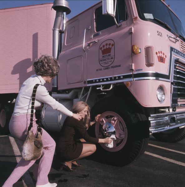 Aileen Baumgardner of Merrillville, Indiana, is looking over the shoulder of Rusty Brda of Schiller Park, Illinois, as she is polishing the chrome discs on the wheel of a pink-colored IH CO-Transtar truck. The women were "Cameo Girls," saleswomen for the Cameo Retail Division of Bestline Incorporated; the company used International C-O-F4070A diesel cabs outfitted with 40-foot trailers to deliver its merchandise.
