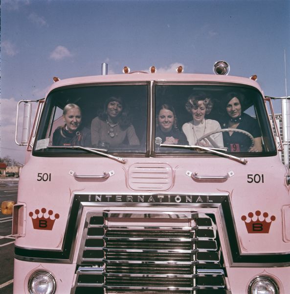 "Cameo Girls," saleswomen for the Cameo Retail Division of Bestline Incorporated, sitting in the cab and looking through the windshield of a pink-colored IH CO-Transtar truck. Bestline used International C-O-F4070A diesel cabs outfitted with 40-foot trailers to deliver its merchandise.
