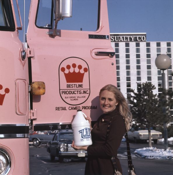 Rusty Brda, a "Cameo Girl" saleswoman with Bestline Incorporated, holding a bottle of Zip All-Purpose Cleaner while standing by the opened door of a pink-colored IH CO-Transtar truck. Bestline used International C-O-F4070A diesel cabs outfitted with 40-foot trailers to deliver its merchandise.
