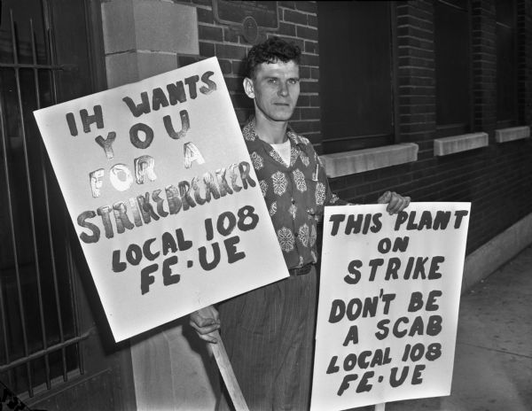 A man, probably Walter Howaniec, stands outside the McCormick Works factory while holding two picket signs during a worker strike.
