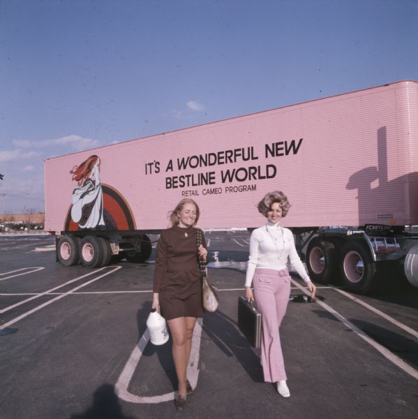 Rusty Brda of Schiller Park, Illinois (left) and Aileen Baumgardner of Merrillville, Indiana, "Cameo Girl" saleswomen for Bestline Incorporated, carrying Bestline products and a briefcase as they are walking away from a pink-colored International Transtar C-O-F4070A diesel truck outfitted with a 40-foot trailer. The text on the trailer reads: "It's a Wonderful New Bestline World; Retail Cameo Division."