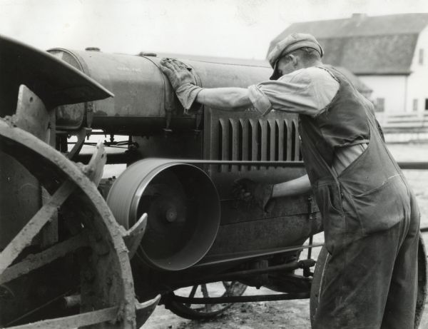 A man wearing overalls and work gloves is reaching through a moving tractor belt on Yeoman Farm to demonstrate a farm hazard. A barn is in the background.
