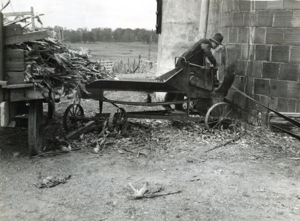 A man is working on silage cutter knives while the machine is in operation, demonstrating a farm hazard.