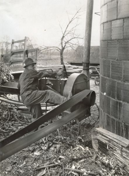 A man is pushing a running belt off a pulley on International Harvester's Hinsdale experimental farm, demonstrating a farm hazard.