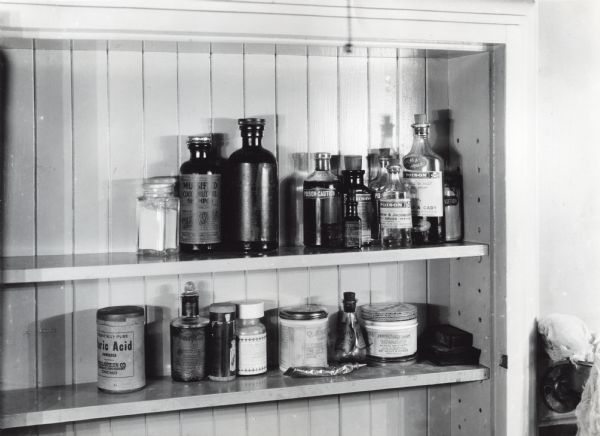 Bottles of poison are stored near medicines and toiletries in a medicine cabinet. The photograph was staged at International Harvester's Hinsdale experimental farm to illustrate farm hazards.