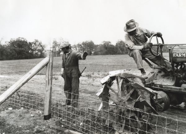 A man is standing and directing another man who is driving a McCormick-Deering Farmall tractor for stretching a fence wire. The photograph was staged on International Harvester's Hinsdale experimental farm to demonstrate a farm hazard.
