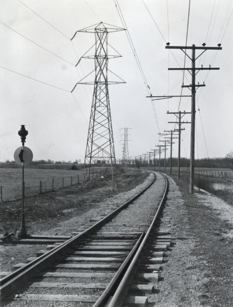 Power lines along both sides of railroad tracks running through a rural area.