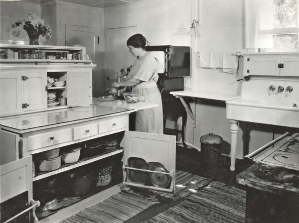 Miss Zearing using a grinder to make bread crumbs inside a farmhouse kitchen.