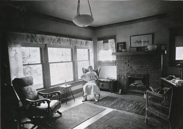Miss Lielle Geddis sitting in a rocking chair while reading an issue of "Country Gentleman" magazine in the living room of her home.