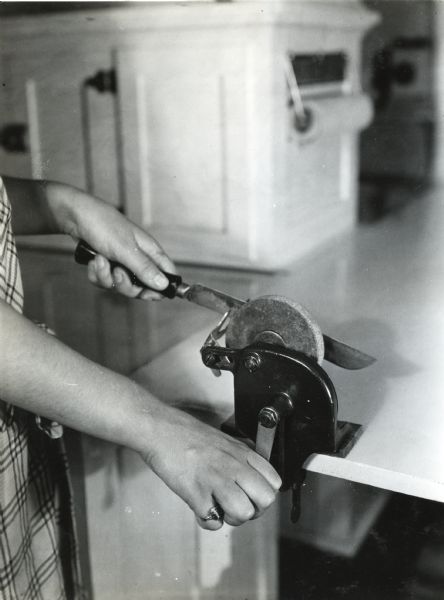 A woman is using a knife sharpener mounted on a kitchen counter to sharpen a blade.