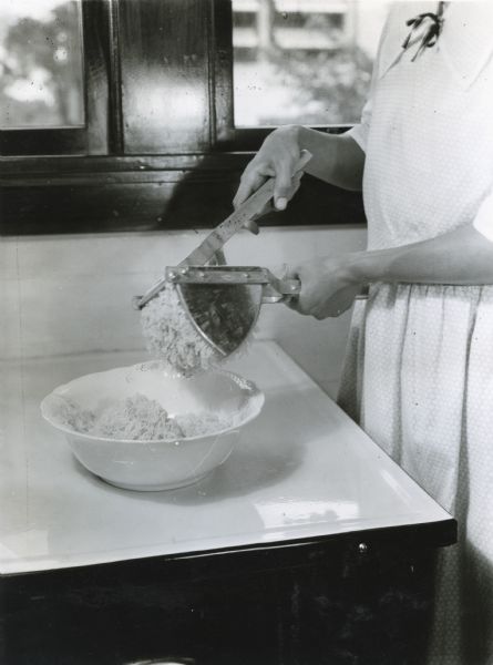 A woman using a potato ricer in a farmhouse kitchen.