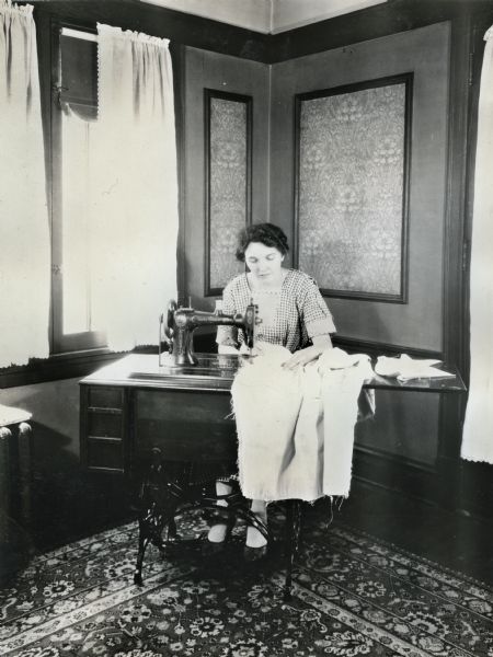 A woman using a foot-pedal sewing machine while working with a piece of fraying fabric.