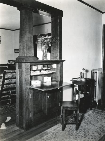 A chair is standing on a rug beside a built-in desk in the home of Adolph Betz. A telephone is sitting on an end table beside the desk.