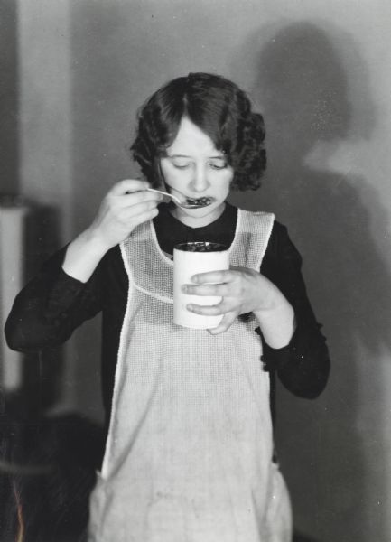 Woman wearing an apron and identified as Anne Jilk is posing with a can of beans to demonstrate the testing of canned food.