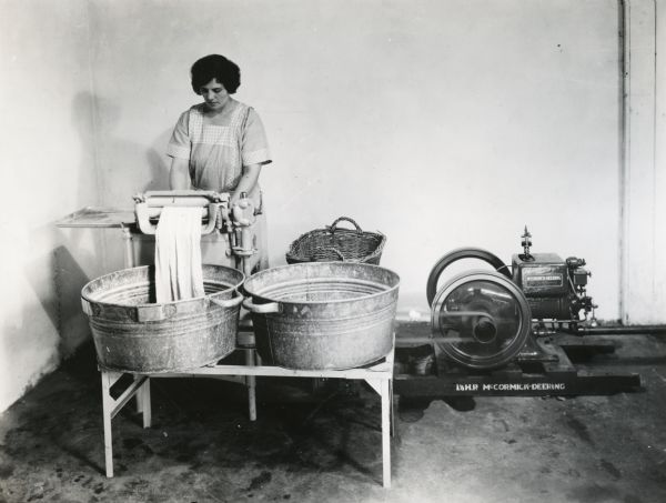 Mrs. Granere using a washing machine powered by a 1.5 horsepower McCormick-Deering engine at International Harvester's Hinsdale experimental farm (Harvester Farm).