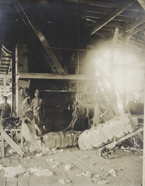 Men baling cotton in a warehouse.