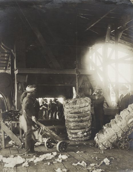 Group of men baling cotton in a warehouse.