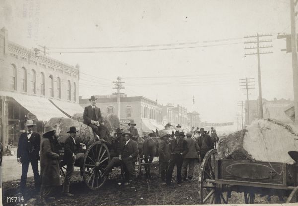 Men on a city street with bales of cotton loaded onto wagons, possibly in Shawnee, Oklahoma.