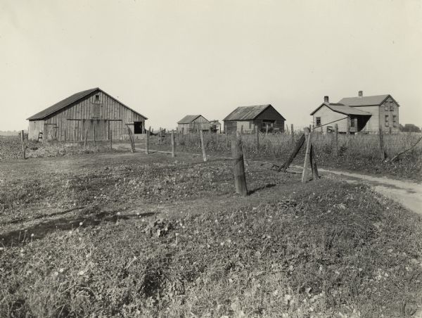 View across a road and field of several rundown farm buildings located near a farmhouse. The image was used to illustre: "poor farm buildings."
